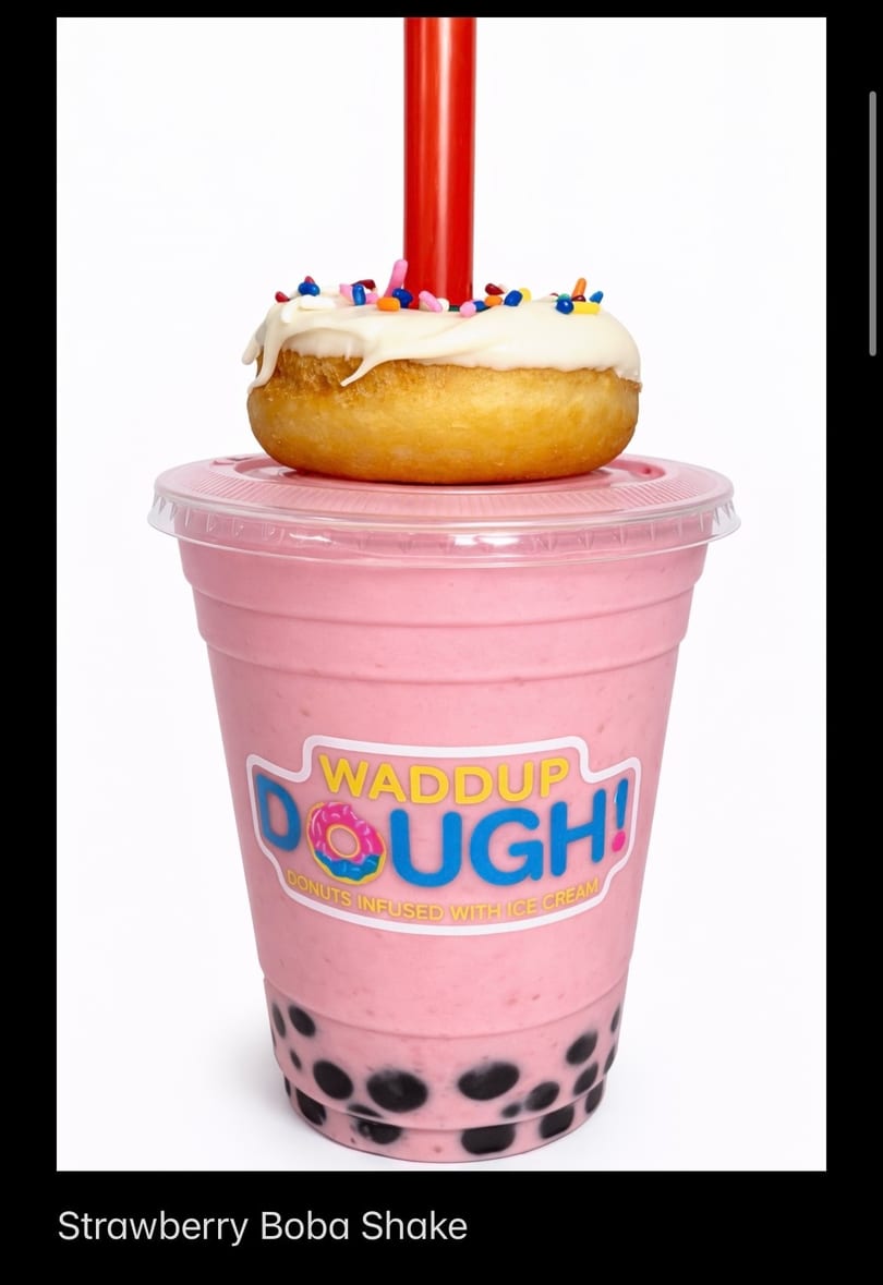 Strawberry boba shake with a white-frosted, sprinkle-covered donut on top, and a red straw.