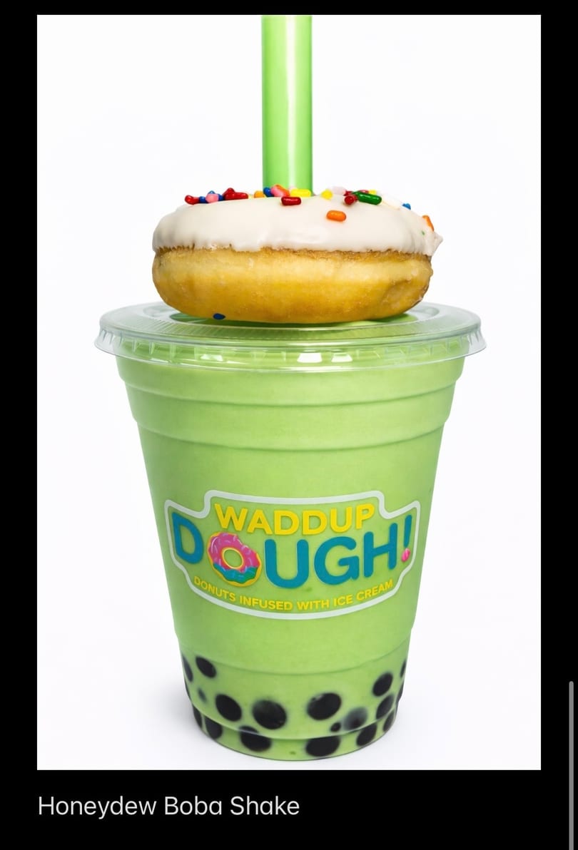 Honeydew boba shake with a white-frosted, sprinkle-covered donut on top, and a green straw.